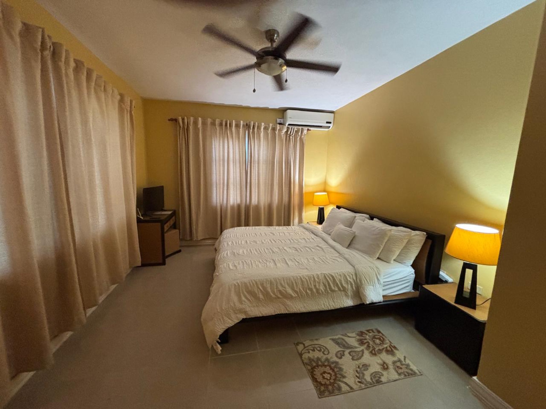 A bedroom with warm yellow walls, a ceiling fan and bedside lamps